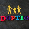 The word 'adoption' spelt out in coloured letters beneath cut-outs of a family