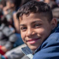 Boy smiling at the camera with the backdrop of a crowd of others