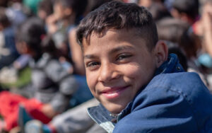 Boy smiling at the camera with the backdrop of a crowd of others