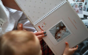 Mother sits and looks photo album with her baby on the background of laid out photos.