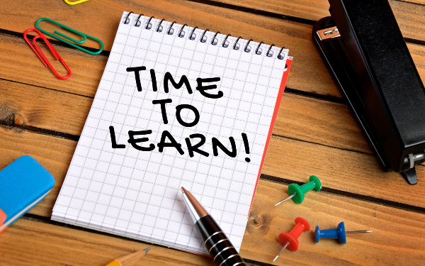 'Time to learn' written on notepad on desk with stapler, paperclips and pins