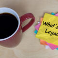 Mug full of coffee next to pile of post-it notes, with the top one reading 'What's your legacy?'