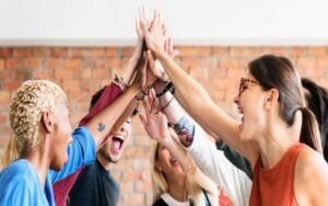 employees in an office high-fiving and looking happy. behind them is a brick wall.