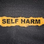 Dark background with crumpled piece of yellow paper with words SELF HARM