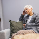 Middle aged woman sitting on the couch (negative emotions). Upset mid-age woman sitting on sofa indoors. She is concerned about something or having headache.