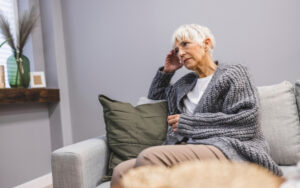 Middle aged woman sitting on the couch (negative emotions). Upset mid-age woman sitting on sofa indoors. She is concerned about something or having headache.