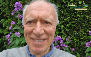 David Howe smiling in front of a wall of purple flowers