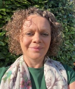 Hannah Thompson, PSW at Walsall. Hannah is looking at the camera and smiling. She has short light brown, curly hair and is wearing a green top with a patterned scarf. It is a sunny day.