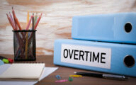 Overtime, Office Binder on Wooden Desk. On the table colored pencils, pen, notebook paper