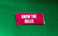 A piece of pink fabric with the words 'know the rules' written on it against a green background