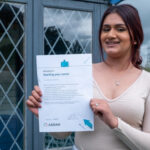 A young woman holding up a certificate for passing a course run by ASDAN