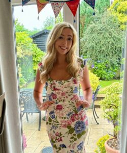 Charlotte posing in front of a window wearing a long dress with flower patterns