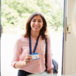 Female care worker smiling as she enters the house of an older woman whom she is greeting
