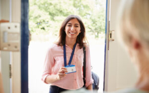 Female care worker smiling as she enters the house of an older woman whom she is greeting