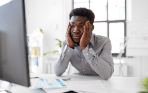 Nervous social worker holding his head in his hands while looking at a computer screen