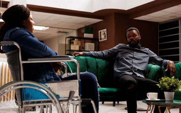 Young black man and woman, who is a wheelchair user, talking in a hotel lobby