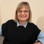 Professor Marian Brandon wearing a black wool vest and a blue shirt, smiling at the camera.
