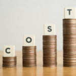Piles of coins of increasing size with tiles spelling out the word 'cost' sitting on each
