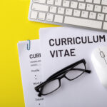 A paper CV on a table alongside a keyboard, mouth and a pair of glasses