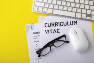 A paper CV on a table alongside a keyboard, mouth and a pair of glasses