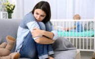 Young mother looking stressed in foreground with baby in cot in background