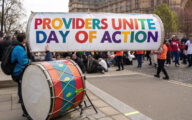 A rally outside the Houses of Parliament with campaigners holding up a banner with the words 'Providers Unite Day of Action'