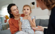 Mother looking at young daughter, who is sitting on her lap, during session with a social worker