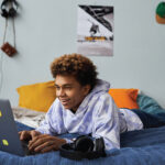 Young man lying on bed looking at his laptop