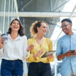 Walking, conversation and business people in office laughing, bonding and talking on lunch break. Happy, friends and group of creative directors with coffee, tablet and phone in workplace together