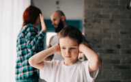 Sad child covering his ears with hands during parents quarrel.