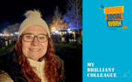 A social worker with long curly red hair, glasses, and a cream knitted hat smiles at an outdoor evening event with lights and people in the background. Beside her, a bright blue graphic features Community Care's “Choose Social Work" campaign logo and the text “My Brilliant Colleague".